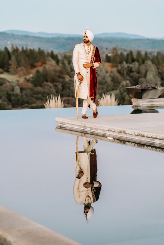 Groom in costume standing by the pool against the backdrop of the mountains.